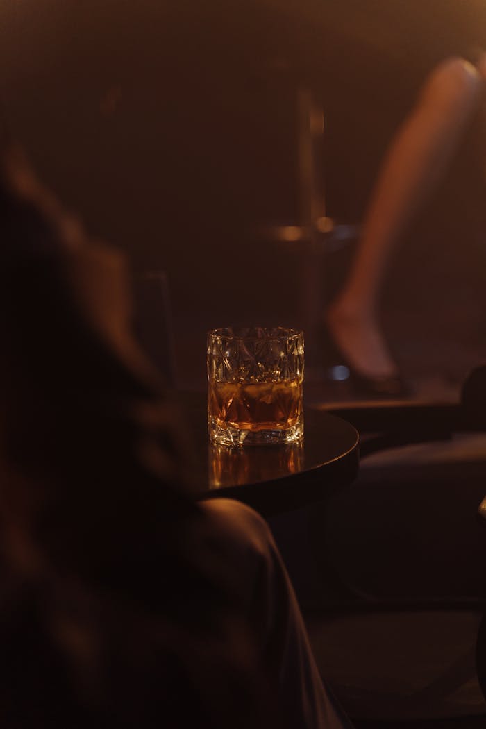A sophisticated whiskey glass with ice in a dimly lit club setting, perfect for nightlife ambiance.