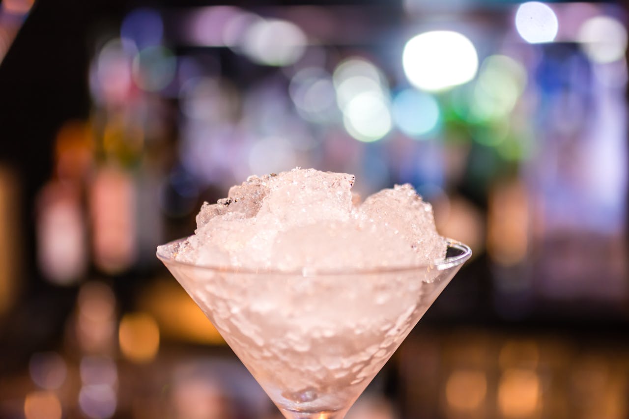 Elegant cocktail glass filled with crushed ice, highlighted by colorful bokeh lights in a nightclub setting.